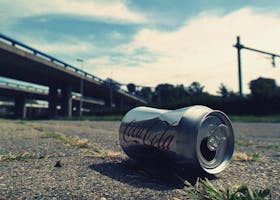 A close-up photo of an empty Coca-Cola can lying on an urban road, symbolizing litter.